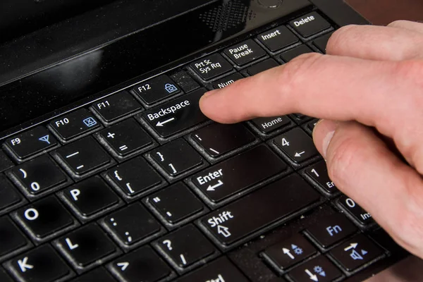 finger presses the backspace key, laptop and hand