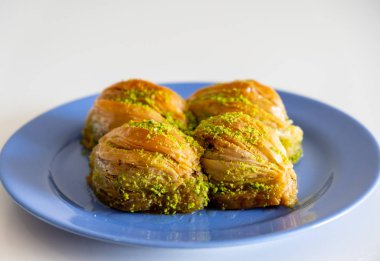 Yeşil Pistachio pudrası ve tereyağı kremalı Türk Midye Baklava 'sı (midye şekilli Baklava). Türk baklavası mavi tabak üzerine