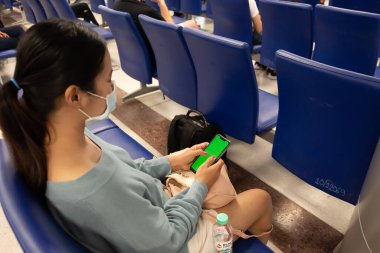 Havaalanındaki Taylandlı kadın telefonda mesaj atıyor. Asyalı kız havaalanında koronavirüs ya da covid 19 için koruma maskesi kullanıyor.. 