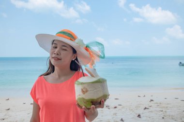 Şirin Asyalı kız sahilde komik surat yapıyor. Taylandlı kadın, turkuaz denizde hindistancevizi suyu içiyor. Tatil gezisi sırasında Tayland 'daki doğal okyanus adasında..