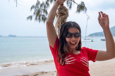 Güneşli bir günde tropik sahilde salıncakta sallanan gülen Taylandlı kadın. Asyalı kız sahilde eğleniyor..
