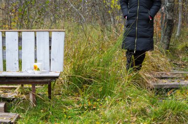 Bir kupa ve kitap bir bankın üzerinde. Yanında da bir parça odaklanmamış insan var.