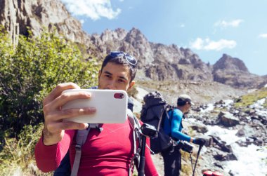 Baba ve oğul Tien Shan dağlarında bir cep telefonuyla selfie çekiyorlar..