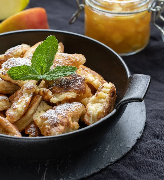 Kaiserschmarrn in a black pan with apples and applesauce in the background