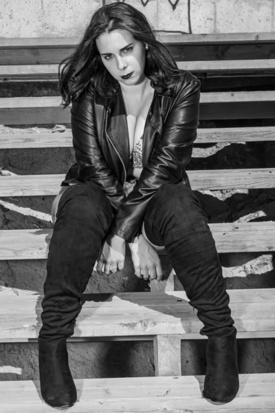 Young woman sitting on stairs with high boots and leather jacket