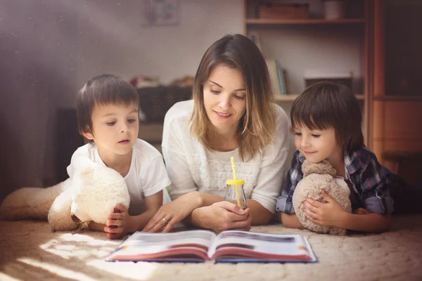 Junge Mutter, lies ihren Kindern, Jungen, im Wohnzimmer ein Buch vor — Stockfoto