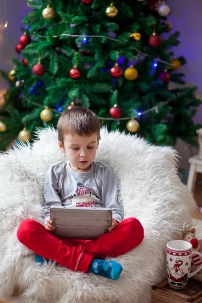 Söt liten sjuk pojke, sitter på böna väska, spelar på Tablet PC — Stockfoto