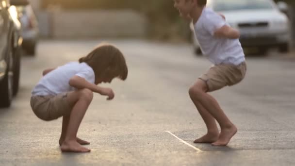 Dos niños dulces, hermanos, jugando con juguetes de coche en la calle en la aldea en la puesta del sol, verano — Vídeos de Stock