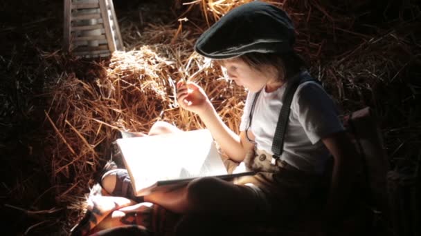 Lieve kind, jongen, lezen van een boek op de zolder op een huis, zittend op een hooi stro eten broodjes bakken — Stockvideo