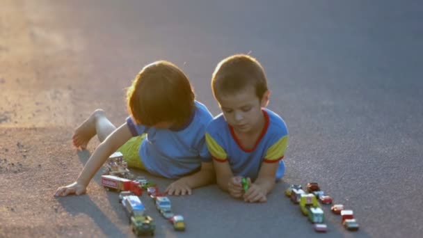 Duas crianças doces, irmãos meninos, brincando com brinquedos de carro na rua na aldeia ao pôr do sol — Vídeo de Stock