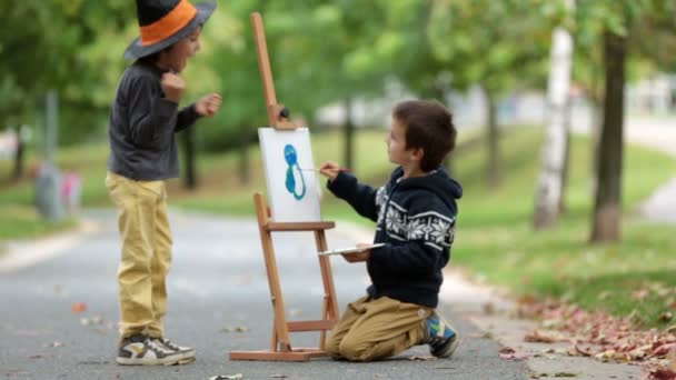 Dos niños dulces, hermanos varones, divirtiéndose pintando juntos en el parque de otoño. Un niño pintar al otro niño, vestido para Halloween — Vídeos de Stock