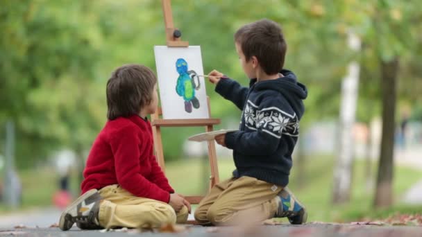 Två söta barn, pojke bröder, har roliga målning i höst park tillsammans. Ett barn måla andra ungen, klädd för halloween — Stockvideo