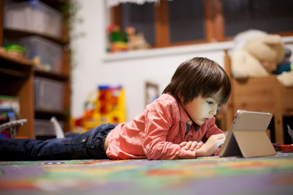 Lindo niño, tirado en el suelo en la habitación de los niños, jugando en la pestaña — Foto de Stock