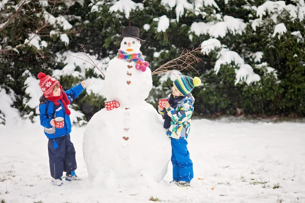 Crianças bonitas felizes, irmãos, construindo boneco de neve no jardim um — Fotografia de Stock