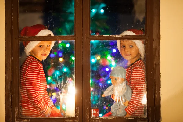 Dos niños, chicos, sentados en una ventana por la noche, uno sosteniendo a —  Fotos de Stock