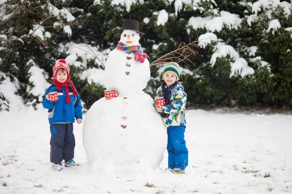 Счастливые красивые дети, братья, строим снеговика в саду — стоковое фото