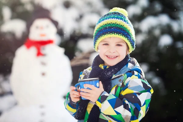 Счастливый красивый ребенок строит снеговика в саду, зимнее время — стоковое фото