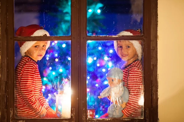 Dos niños, chicos, sentados en una ventana por la noche, uno sosteniendo a —  Fotos de Stock
