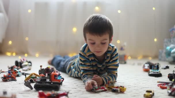 Little child playing with lots of colorful plastic toys indoor, building different cars and objects on Christmas — Stock Video