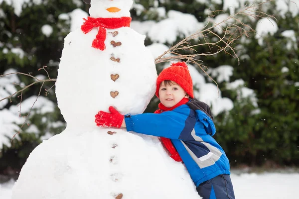 Feliz niño hermoso edificio muñeco de nieve en el jardín, tiempo de invierno —  Fotos de Stock