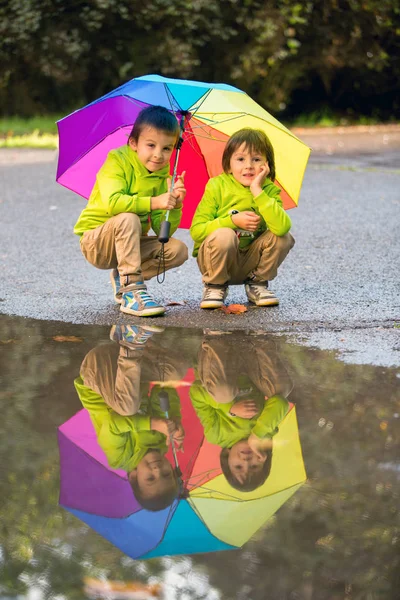 เด็กน้อยที่น่ารักสองคน เล่นในสวนสาธารณะในวันที่ฝนตก เล่น — ภาพถ่ายสต็อก