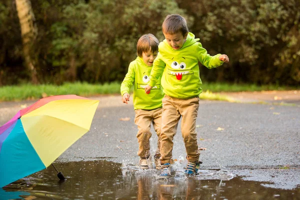 दोन मोहक लहान मुले, पावसाळ्यात एका उद्यानात खेळत, खेळतात — स्टॉक फोटो, इमेज