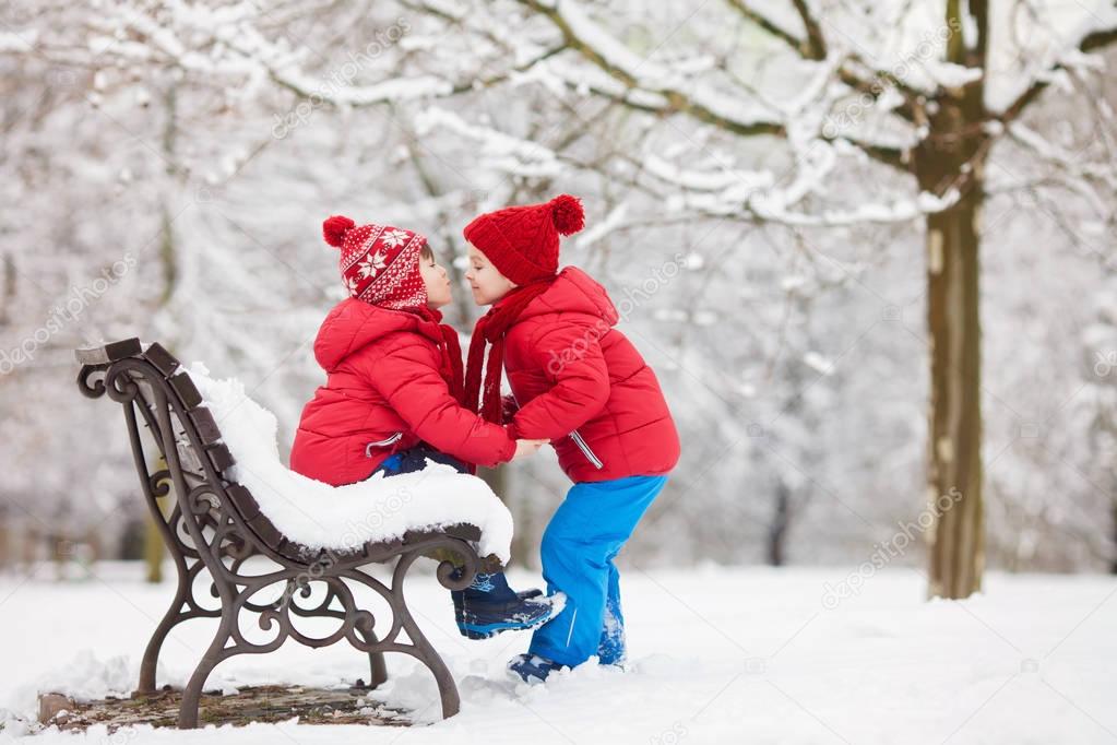 Two adorable children, boy brothers, playing in a snowy park, ho