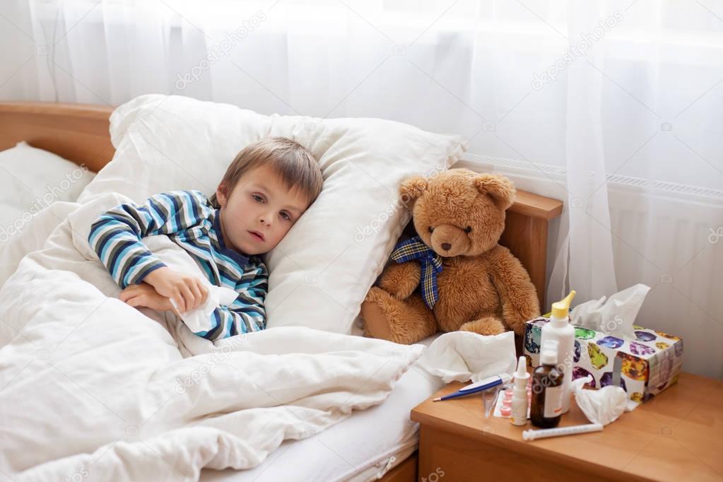 Sick child boy lying in bed with a fever, resting