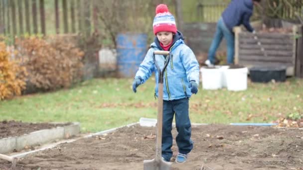 Liten pojke, skotta i trädgården, gräva hösten tid — Stockvideo