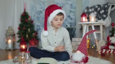 Sevimli okul öncesi çocuk, çocuk, bir kitap okuma ve açık havada kar yağışı sırasında evde kurabiye yemek