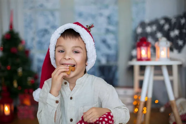 Lindo niño preescolar, niño, leyendo un libro y comiendo galletas en — Foto de Stock