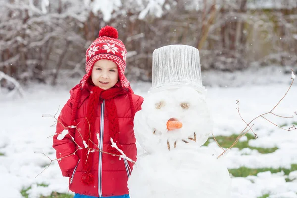 Милый мальчик, строит снеговика в саду, веселится — стоковое фото