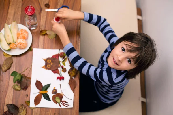 Doce criança, menino, aplicando folhas usando cola enquanto faz artes e — Fotografia de Stock