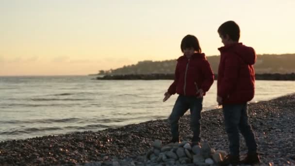 Dos niños, jugando en la playa con rocas, invierno al atardecer — Vídeos de Stock