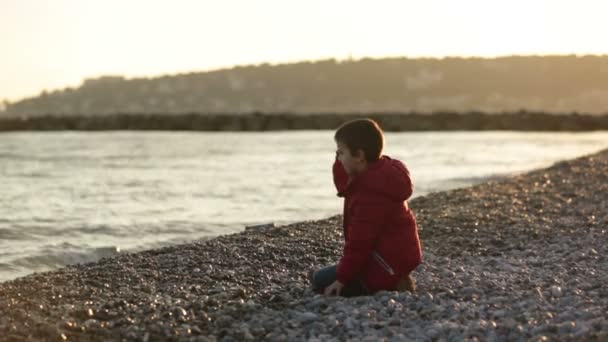 Dos niños, jugando en la playa con rocas, invierno al atardecer — Vídeos de Stock