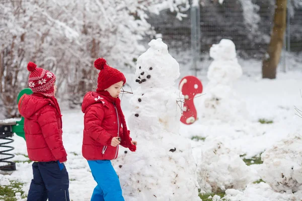 Glada vackra barn, bröder, bygga snögubbe i trädgården — Stockfoto
