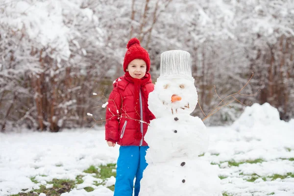 Söt pojke, bygga en snögubbe i en trädgård, ha roligt — Stockfoto