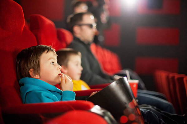 Father and two children, boys, watching cartoon movie in the cin