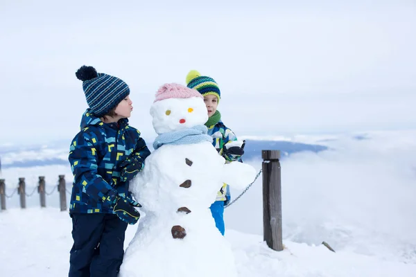 Criança bonito, construindo boneco de neve e brincando com ele no topo do monte — Fotografia de Stock