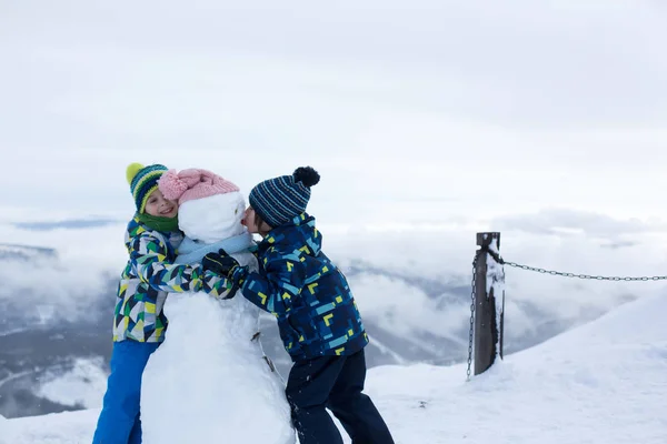 Двое детей, строящих снеговика на вершине горы — стоковое фото