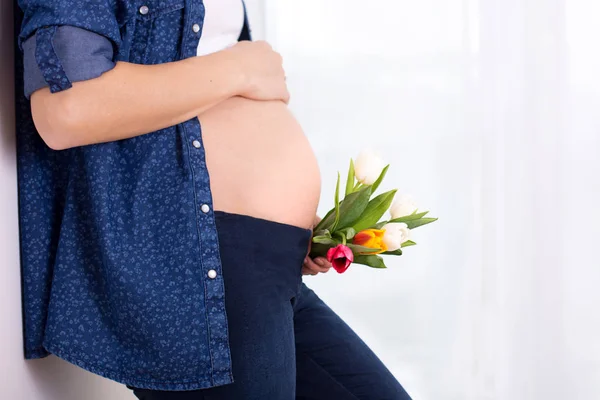 Молодая беременная женщина, держащая цветы тюльпана, опираясь на стену — стоковое фото