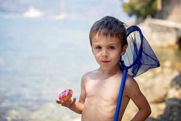 Dolce ritratto di un ragazzo, mangiare ciambella sulla spiaggia — Foto Stock