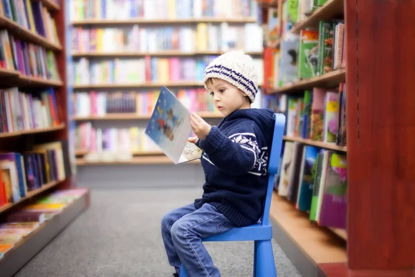 Entzückender kleiner Junge, der in einer Buchhandlung sitzt — Stockfoto