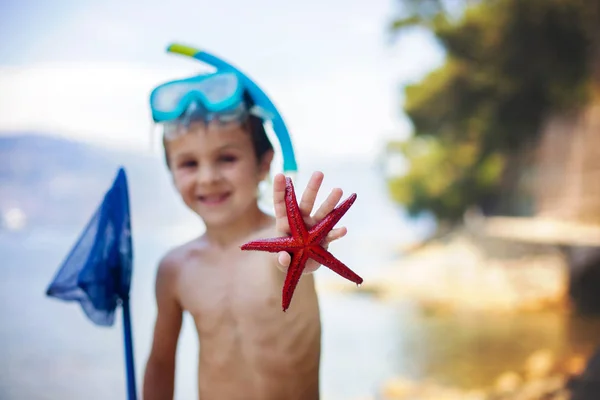 Petit garçon tenant dans ses mains une étoile de mer rouge à cinq pointes et un filet — Photo