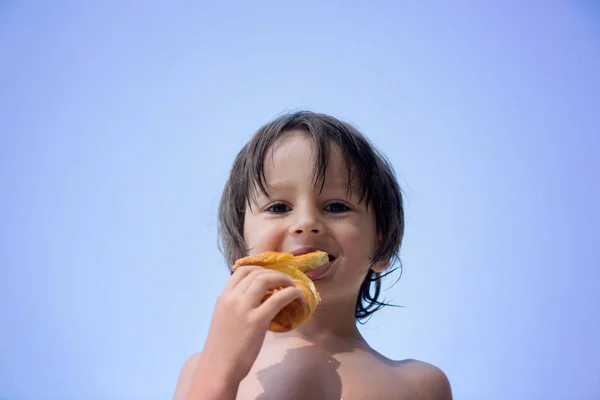 可爱的孩子，男孩，在海滩上吃牛角面包 — 图库照片
