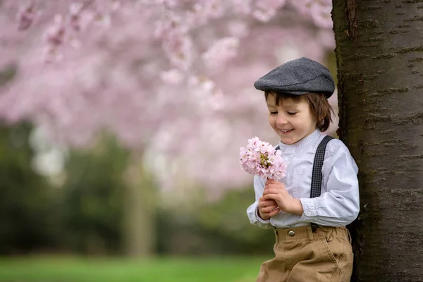 Красивий молодий хлопчик дошкільного віку, що стоїть у вишневому квітучому саду — стокове фото