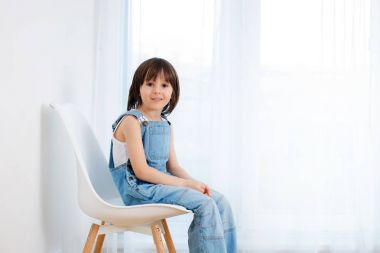 Cute child, sitting on white chair at home clipart