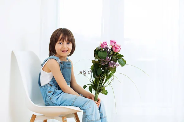 Süße kleine Kind, Junge, sitzt auf einem Stuhl zu Hause, hält flo — Stockfoto