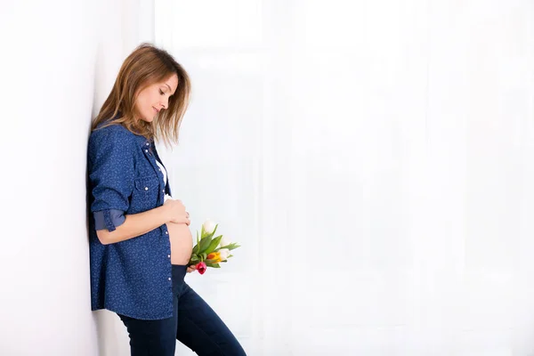 Fiatal terhes nő, gazdaság tulipán virág, támaszkodva a fal — Stock Fotó