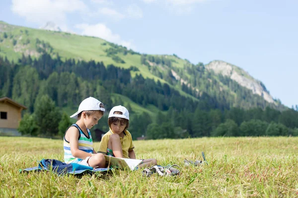 Zwei niedliche Kinder, die auf einer Liegewiese in den Schweizer Alpen ein Buch lesen — Stockfoto
